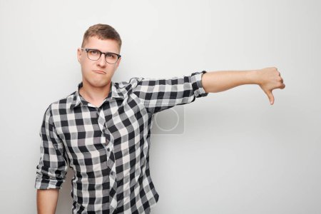 Photo for Portrait of man in shirt and glasses showing thumbs down isolated on white studio background. Dislike, wrong choice, negative evaluation concep - Royalty Free Image
