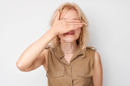 Téléchargez les photos : Portrait de femme couvrant les yeux à la main isolé sur fond de studio blanc - en image libre de droit