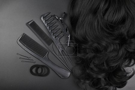Téléchargez les photos : Outils de coiffure close-up isolé sur fond noir. Boucles de cheveux bruns foncés et un ensemble de peignes, clips, épingles à cheveux, concept de salon de beauté pour cheveux - en image libre de droit