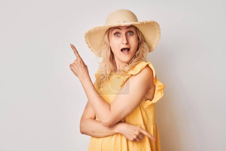 Téléchargez les photos : Belle femme mature de 50 ans pointant du doigt, démontrant un espace vide pour le produit ou le texte isolé sur fond de studio blanc - en image libre de droit
