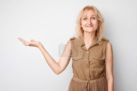 Foto de Hermosa mujer madura de 50 años sosteniendo algo en la mano, demostrando espacio vacío para el producto o el texto aislado en el fondo del estudio blanco - Imagen libre de derechos