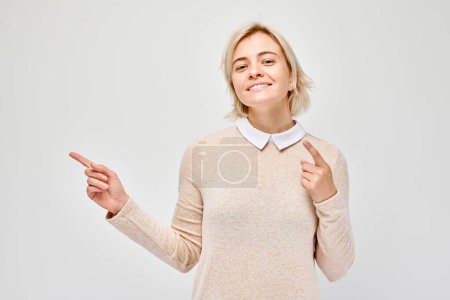 Photo for Young blond woman in casual pointing aside finger, demonstrating empty space for product or text isolated on white studio backgroun - Royalty Free Image