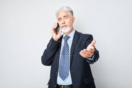 Téléchargez les photos : Portrait d'un homme d'affaires âgé en costume parlant sur un téléphone portable. Personne avec smartphone isolé sur fond blanc - en image libre de droit
