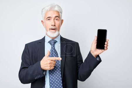Photo for Portrait of elderly businessman in suit showing blank mobile phone screen with excited face. Person with smartphone isolated on white backgroun - Royalty Free Image
