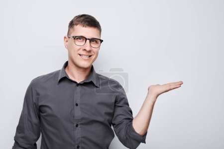 Photo for Handsome man in glasses holding something in hand, demonstrating empty space for product or text isolated on white studio backgroun - Royalty Free Image