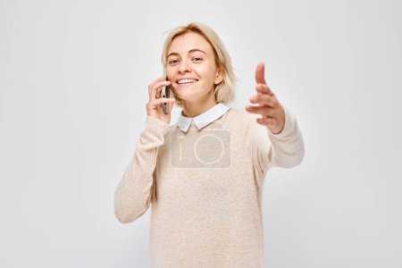 Foto de Retrato de una joven rubia hablando por teléfono móvil con cara feliz y sonriente. Persona con teléfono inteligente aislado en el fondo blanco - Imagen libre de derechos