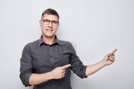 Foto de Hombre guapo en gafas señalando a un lado el dedo, demostrando espacio vacío para el producto o el texto aislado en fondo de estudio blanco - Imagen libre de derechos
