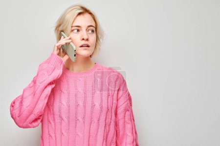 Téléchargez les photos : Portrait de jeune femme blonde en pull rose parlant sur téléphone portable avec un visage souriant heureux. Personne avec smartphone isolé sur fond blanc - en image libre de droit