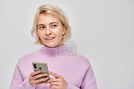 Photo for Portrait of young blond woman holding mobile phone in hand with happy smiling face. Person with smartphone isolated on white backgroun - Royalty Free Image