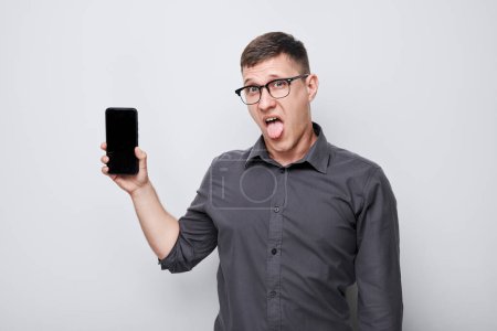 Téléchargez les photos : Portrait de jeune homme d'affaires montrant écran vierge de téléphone portable avec visage excité. Personne avec smartphone isolé sur fond blanc - en image libre de droit