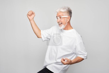 Téléchargez les photos : Portrait de visage souriant homme aux cheveux gris serrant les poings et se réjouissant, célébrant la victoire isolé sur fond de studio blanc, banne publicitaire - en image libre de droit