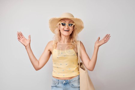 Photo for Portrait mature blond woman with sunglasses, hat, shopping bag celebrating vacation, jumping, dancing having fun isolated on white studio backgroun - Royalty Free Image