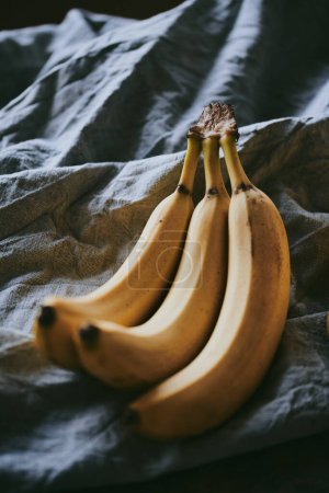Téléchargez les photos : Gros plan d'un bouquet de bananes sur un fond de tissu sombre - en image libre de droit