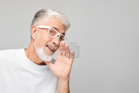 Téléchargez les photos : Portrait d'homme âgé en blanc criant bruyamment avec les mains, les nouvelles, les paumes pliées comme un mégaphone isolé sur fond blanc - en image libre de droit