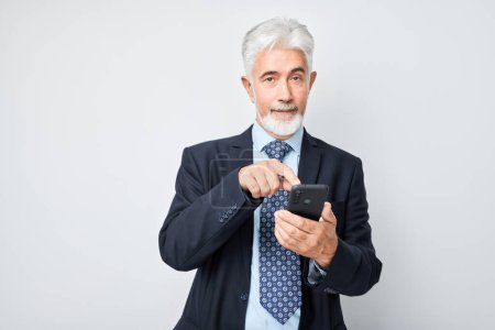 Foto de Retrato de hombre de negocios de edad avanzada en traje que muestra la pantalla del teléfono móvil en blanco con la cara emocionada. Persona con teléfono inteligente aislado en el fondo blanco - Imagen libre de derechos