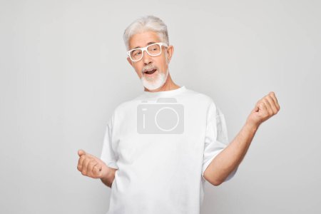 Foto de Retrato de cara sonriente hombre de pelo gris apretando puños y regocijo, celebrando la victoria aislado en el fondo del estudio blanco, banne publicidad - Imagen libre de derechos