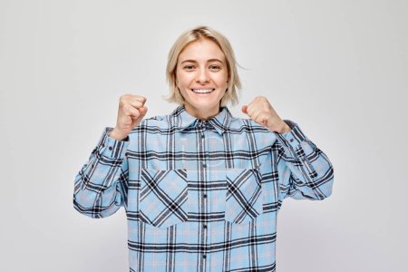 Téléchargez les photos : Portrait de visage souriant jeune femme blonde serrant les poings et se réjouissant, célébrant la victoire isolée sur fond de studio blanc, banne publicitaire - en image libre de droit