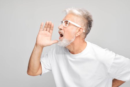 Foto de Retrato de hombre mayor en blanco gritando fuerte con las manos, noticias, palmas dobladas como megáfono aislado sobre fondo blanco - Imagen libre de derechos