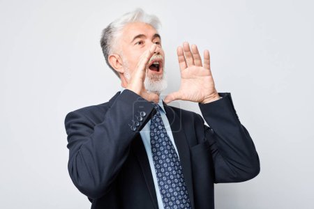 Foto de Retrato de un hombre de negocios mayor con traje gritando fuerte con las manos, noticias, palmas dobladas como megáfono aislado sobre fondo blanco - Imagen libre de derechos