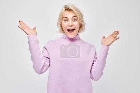 Foto de Retrato rubia joven feliz cara sonriendo alegremente con las palmas levantadas y la boca abierta conmocionada aislado en fondo de estudio blanco - Imagen libre de derechos