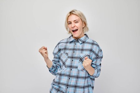 Photo for Portrait of smiling face blond young woman clenching fists and rejoicing, celebrating victory isolated on white studio background, advertising banne - Royalty Free Image