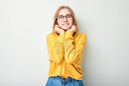 Foto de Mujer joven sonriente en suéter amarillo y gafas, posando sobre un fondo claro. - Imagen libre de derechos