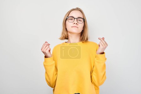 Foto de Mujer joven en suéter amarillo cruzando los dedos para la buena suerte, aislado sobre fondo gris. - Imagen libre de derechos