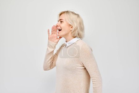 Téléchargez les photos : Portrait de fille blonde criant bruyamment avec les mains, nouvelles, paumes pliées comme un mégaphone isolé sur fond blanc - en image libre de droit