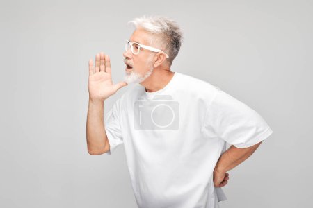 Téléchargez les photos : Portrait d'homme âgé en blanc criant bruyamment avec les mains, les nouvelles, les paumes pliées comme un mégaphone isolé sur fond blanc - en image libre de droit