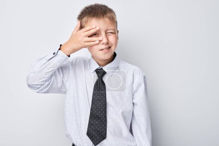 Foto de Niño joven en camisa y corbata cubriendo su cara con la mano, lúdico gesto peekaboo. - Imagen libre de derechos