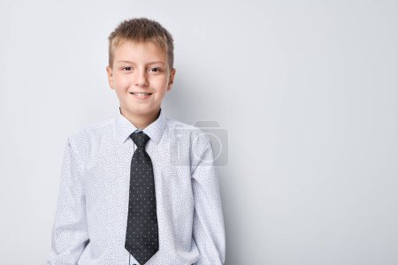 Téléchargez les photos : Jeune garçon souriant en chemise et cravate debout sur un fond uni avec espace de copie. - en image libre de droit