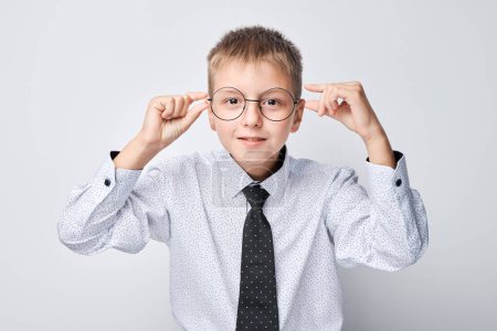 Photo for Smiling boy adjusting glasses, wearing shirt and tie on white background. - Royalty Free Image