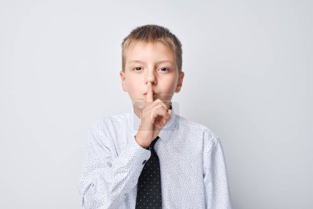 Téléchargez les photos : Portrait de garçon en uniforme scolaire montre shhh geste silence, taisez-vous, ne dites pas secret - en image libre de droit