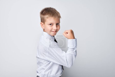 Photo for Confident young boy in white shirt showing muscles on plain background, strength and growth. - Royalty Free Image