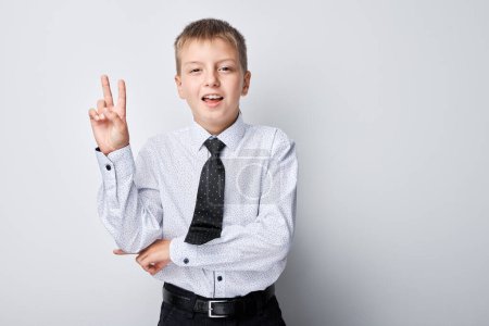 Téléchargez les photos : Portrait de garçon en uniforme scolaire montre geste de paix et d'amour avec expression faciale positive - en image libre de droit