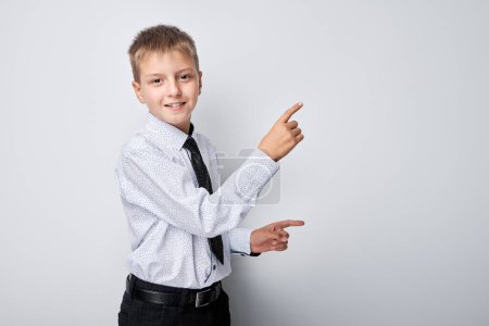 Téléchargez les photos : Portrait garçon en uniforme scolaire pointant du doigt l'espace vide pour la publicité des produits ou du texte - en image libre de droit