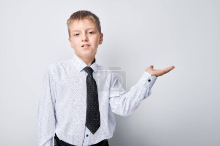 Téléchargez les photos : Jeune garçon en chemise et cravate présentant à la main, isolé sur fond blanc. - en image libre de droit