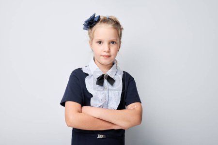 Foto de Niña confiada posando con los brazos cruzados sobre fondo claro, vistiendo uniforme escolar - Imagen libre de derechos
