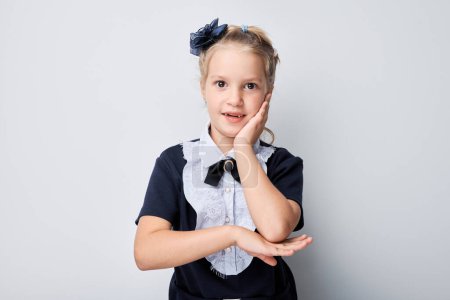 Photo for Surprised young girl with hands on cheeks against a gray background, expressing shock and amazement - Royalty Free Image