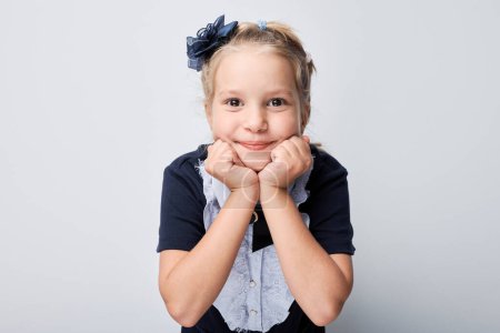 Foto de Retrato de niña sonriente con diadema azul apoyando la barbilla en las manos sobre un fondo gris. - Imagen libre de derechos