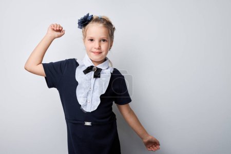 Téléchargez les photos : Confiant jeune fille posant avec le poing levé portant l'uniforme de l'école et bandeau bleu - en image libre de droit