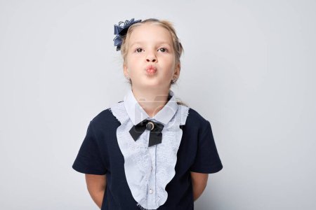 Photo for Adorable girl in school uniform making a kissing face against a light grey background. - Royalty Free Image