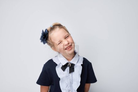 Foto de Jovencita alegre guiñando un ojo, con un arco y uniforme escolar sobre un fondo claro. - Imagen libre de derechos