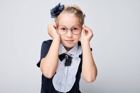 Photo for Girl adjusting glasses dressed in smart attire with bow and headband isolated on light background - Royalty Free Image