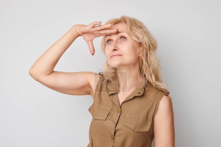 Photo for Woman looking into distance with hand above eyes, neutral background. - Royalty Free Image