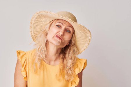 Téléchargez les photos : Femme en chemisier jaune et chapeau de paille avec une expression coûteuse, isolée sur un fond clair. - en image libre de droit