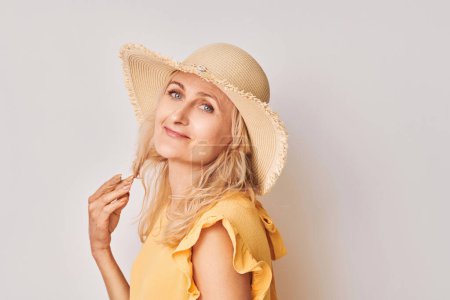 Foto de Mujer sonriente en top amarillo y sombrero de paja posando juguetonamente sobre un fondo claro. - Imagen libre de derechos