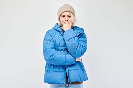 Téléchargez les photos : Femme en veste d'hiver bleue et bonnet avec une expression réfléchie, isolé sur un fond clair. - en image libre de droit