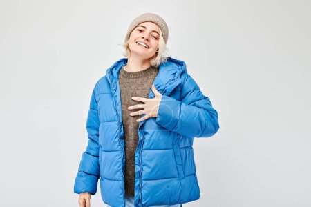 Téléchargez les photos : Personne souriante en tenue d'hiver avec bonnet et veste gonflante bleue, le contenu de recherche et confortable. - en image libre de droit