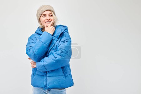 Photo for Woman in winter attire with a pensive expression, isolated on a light background. - Royalty Free Image